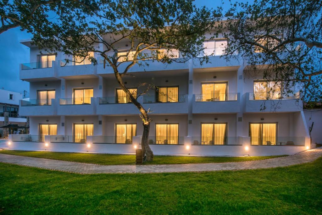 a large white building with a tree in front of it at South Coast Hotel in Makry Gialos