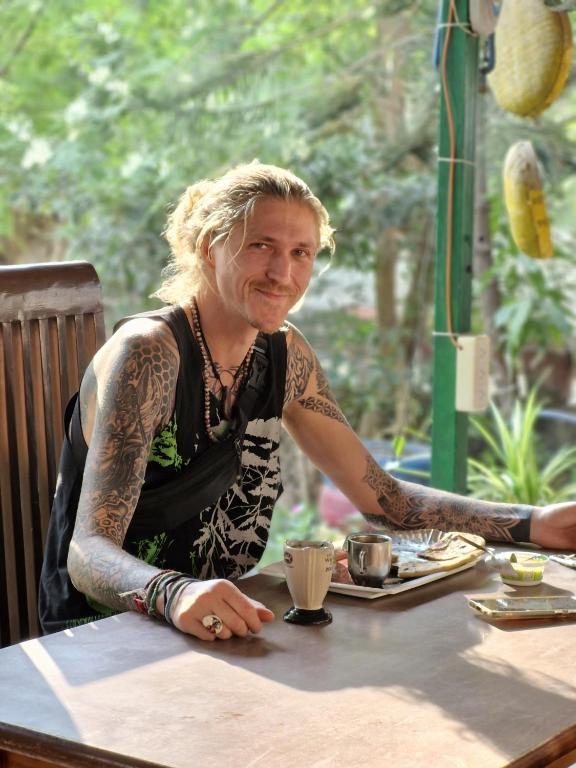 a man with tattoos sitting at a table at Dream Vision Guest House in Diu