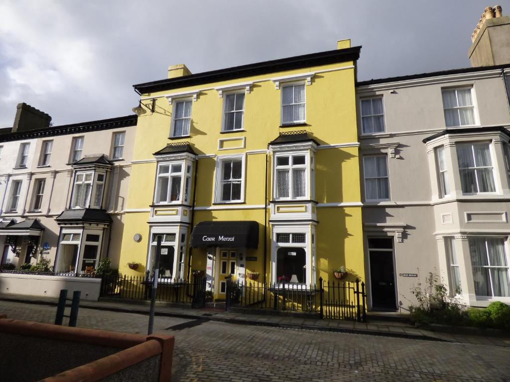 ein gelbes Haus auf einer Straße mit weißen Gebäuden in der Unterkunft Caer Menai in Caernarfon