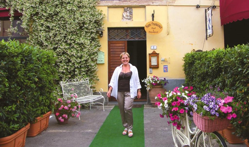 Bed and Breakfast San Francesco في Buti: a woman walking down a green path in front of a house