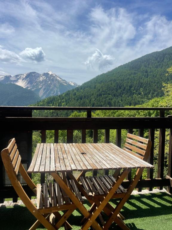 une table et des chaises en bois sur un balcon avec des montagnes dans l'établissement Le Petit Torrent, à Pra-Loup
