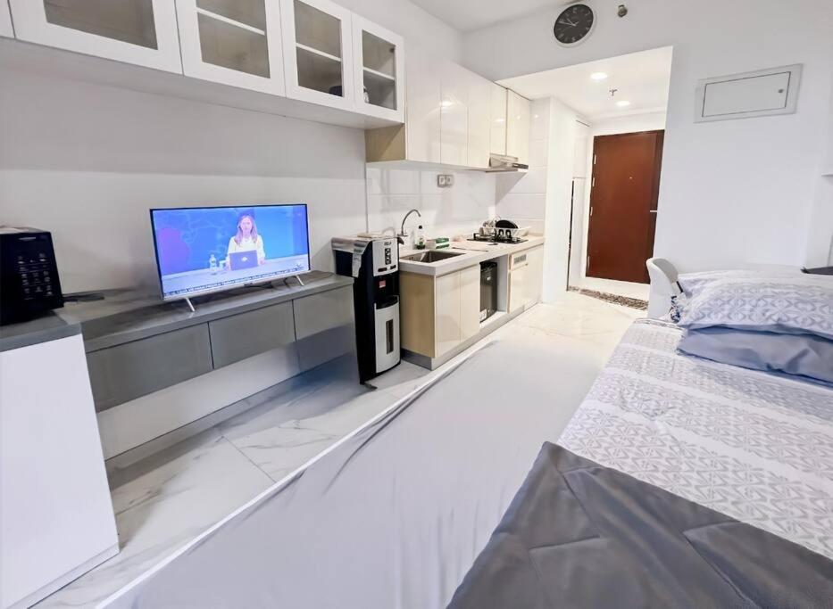a white bedroom with a bed and a tv on a counter at Cozy Studio Skyhouse Apt near ICE BSD with pool & Gym by 2ndHome in Cilenggang