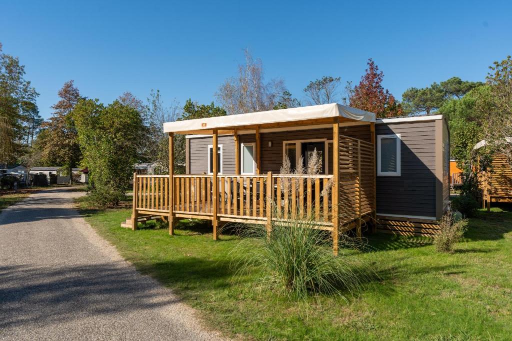 une petite cabine avec une terrasse sur une pelouse dans l'établissement CAMPING LES OURMES, à Hourtin