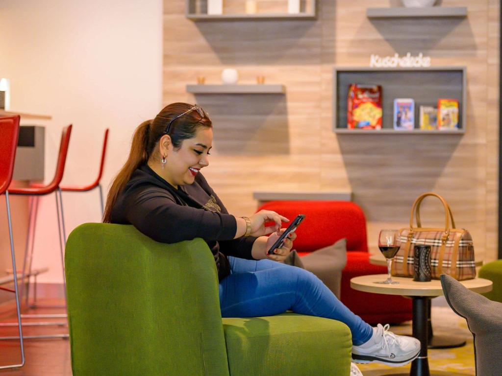 a woman sitting in a green chair looking at her cell phone at ibis Stuttgart Airport Messe in Leinfelden-Echterdingen