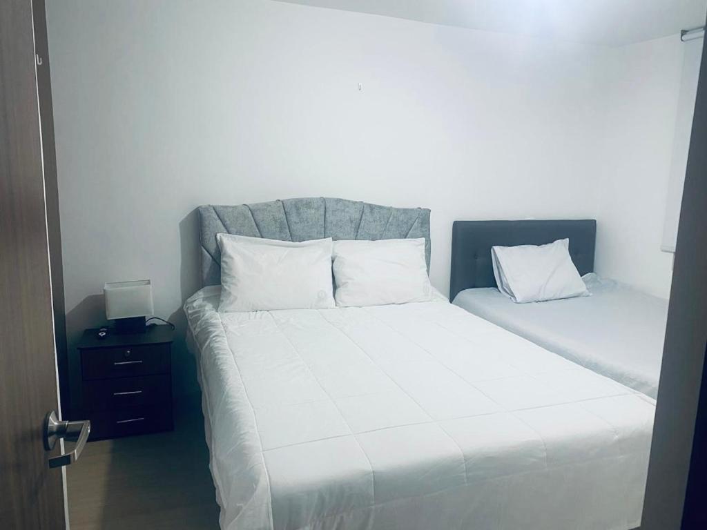 a bedroom with two beds with white sheets and pillows at Aparta-hotel Eskala UPTC in Tunja