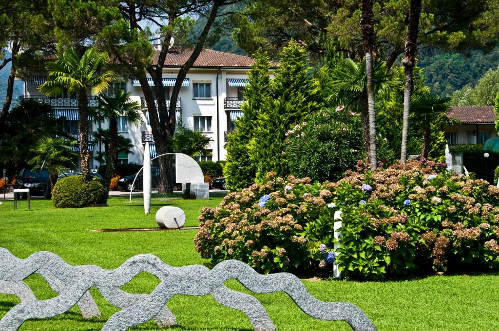 a sculpture in a park with a building and flowers at Villa Delta - Parkhotel Delta in Ascona