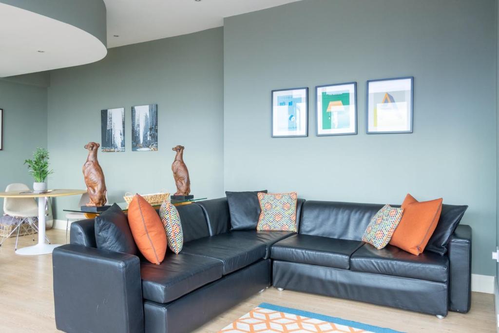 a black leather couch in a living room with orange pillows at GuestReady - Enchanting views from Millenium Tower in Dublin