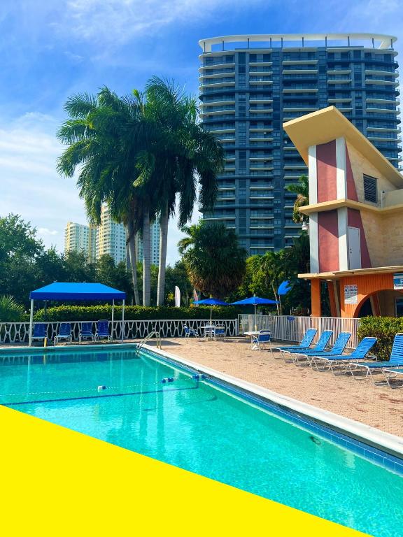 a swimming pool with chairs and palm trees and a building at Bposhtels Hollywood Florida in Hollywood