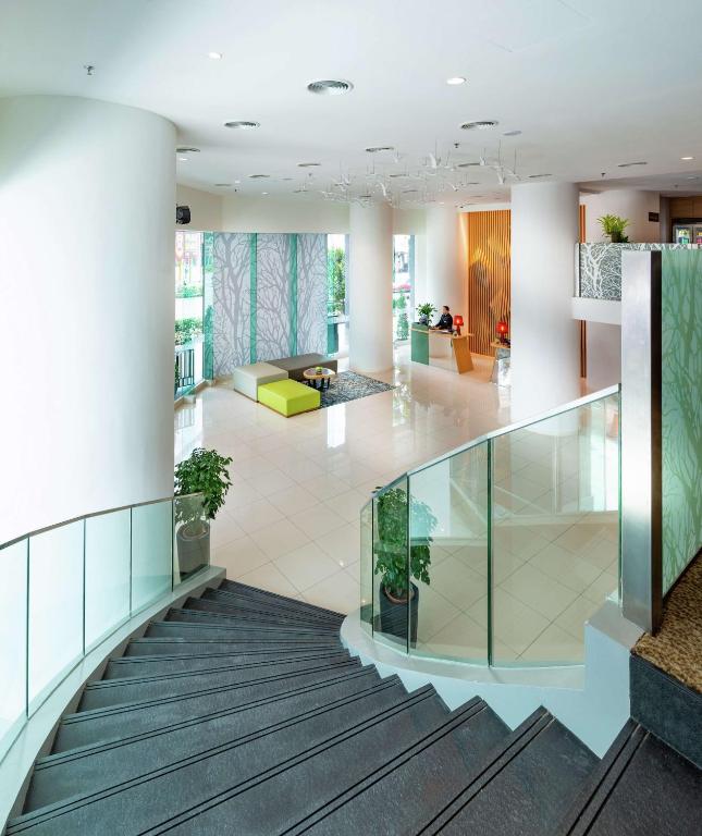 A sweeping staircase opens onto a bright, modern lobby with glass railings and colorful seating.