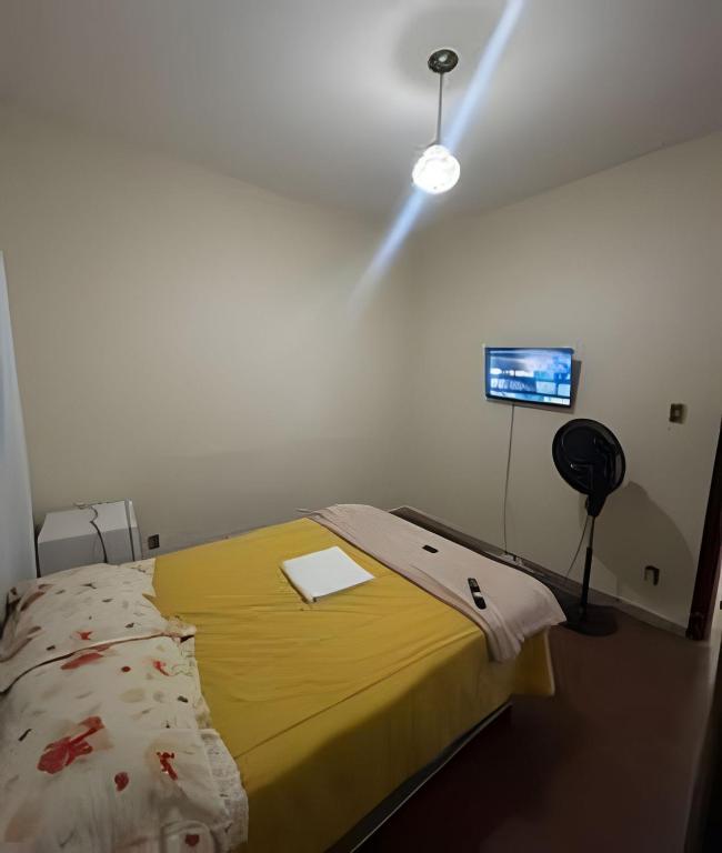 a room with a bed with a yellow blanket and a television at Casa 5 quartos entre Centro e Pampulha in Belo Horizonte