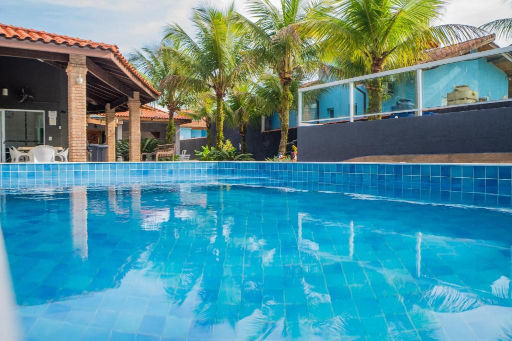 a swimming pool in front of a house with palm trees at Casa com piscina aquecida, Condomínio a beira mar in Bertioga