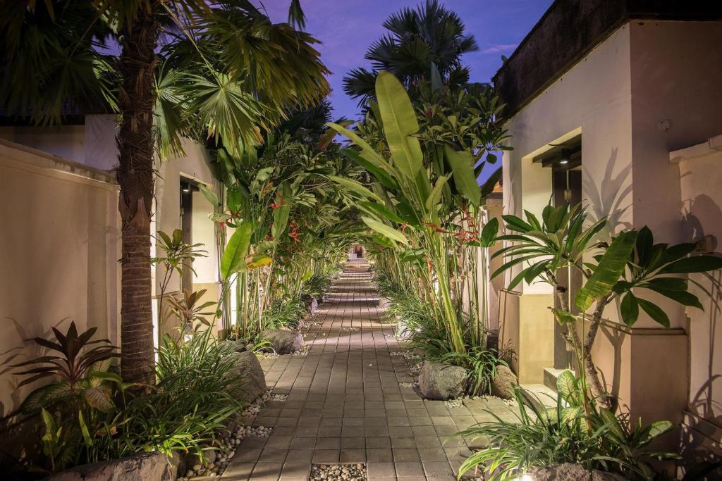 a walkway between two buildings with palm trees at The Tukad Villa in Seminyak