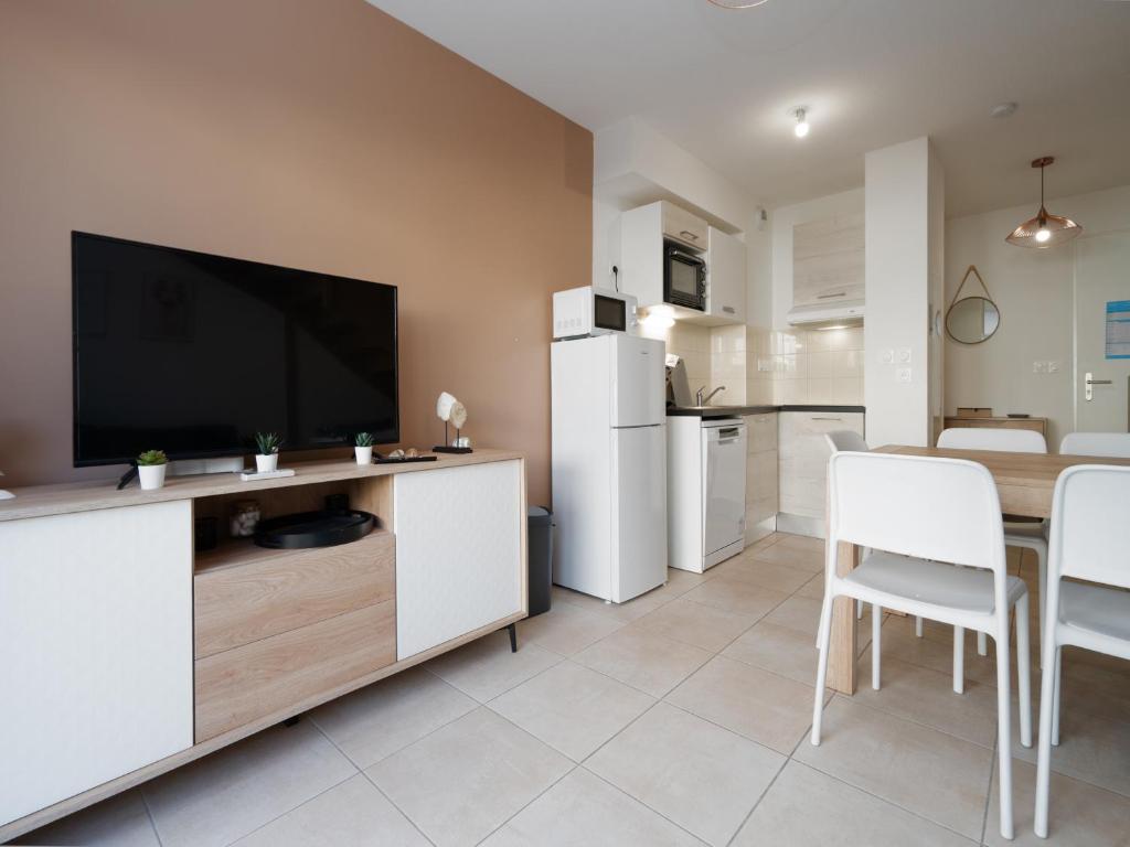 Il comprend un salon doté d'une télévision et d'une table avec des chaises blanches. dans l'établissement La Dune N 59 - Villa 3P6, à Sérignan