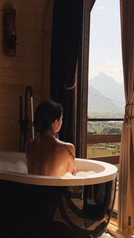 a man sitting in a bath tub looking out a window at Outdoor Cottages Kazbegi in Kazbegi