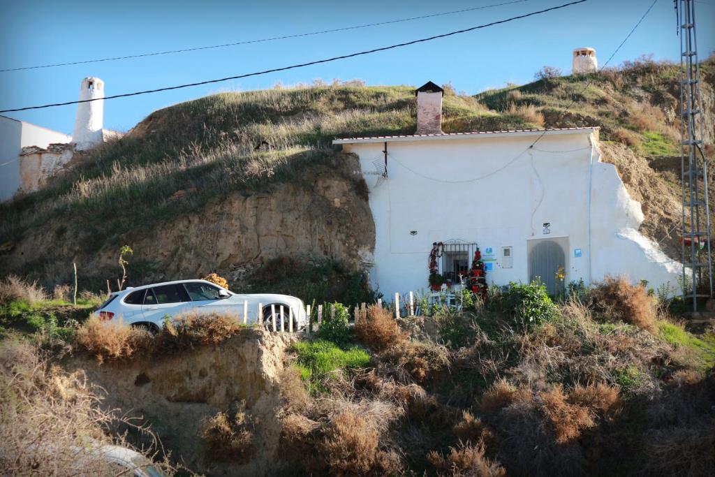 a white car parked in front of a house on a hill at Cueva La Loli in Guadix