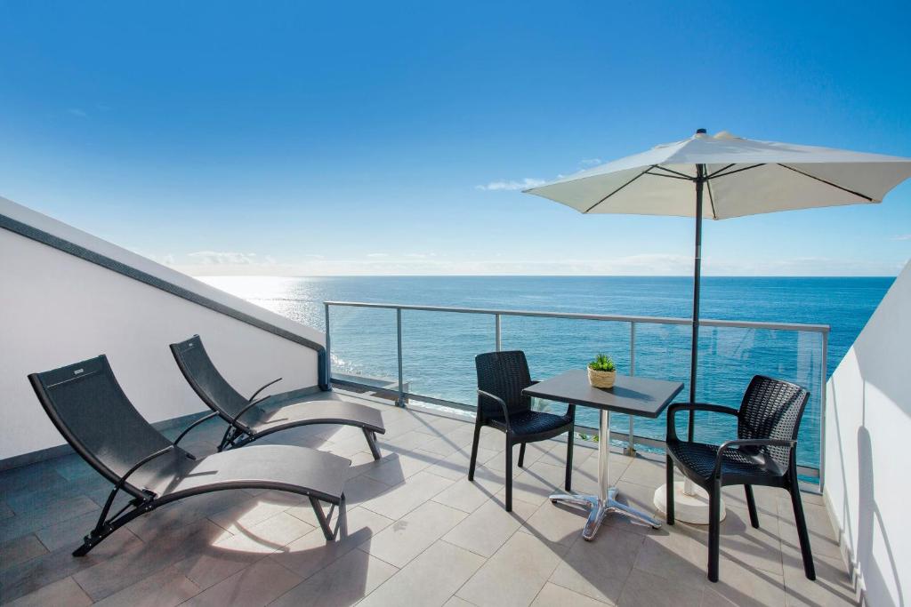 Un balcón con una mesa y sillas y una sombrilla. en The Wave House - Oceanfront, en Jardim do Mar