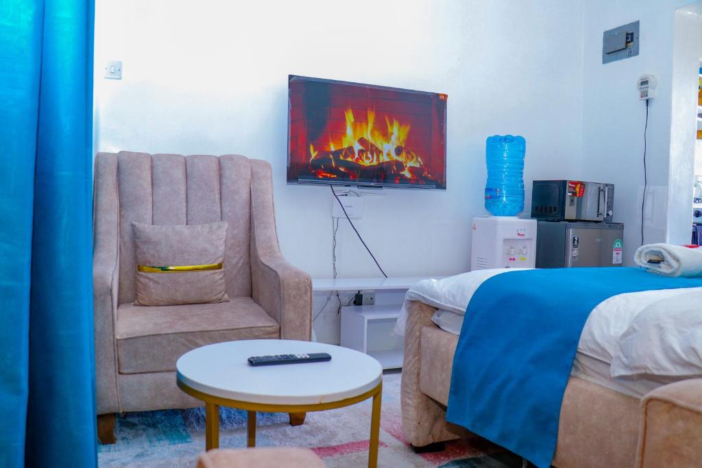 a bedroom with a bed and a chair and a tv at Haydenco Suites Signatuture Mall Syokimau in Nairobi