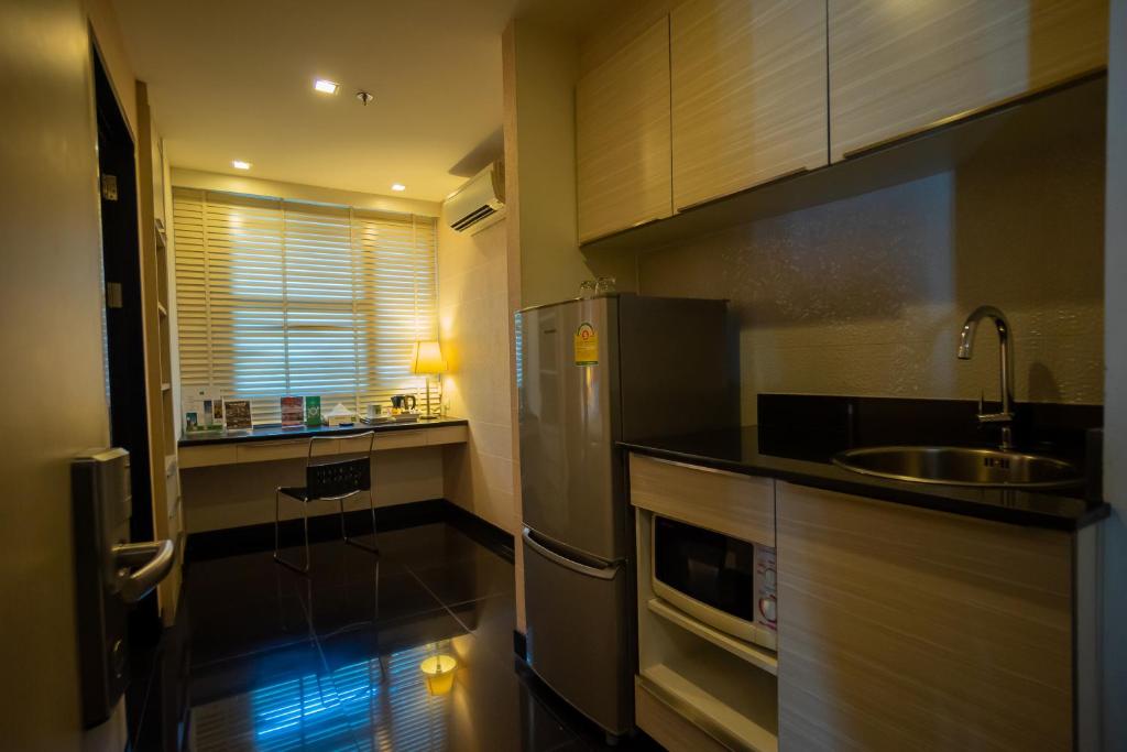 A compact kitchenette with a refrigerator, microwave, sink and small desk by the window.