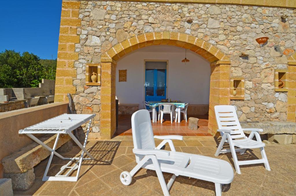 a patio with white chairs and a table and a stone building at Casa Orizzonte in Patù