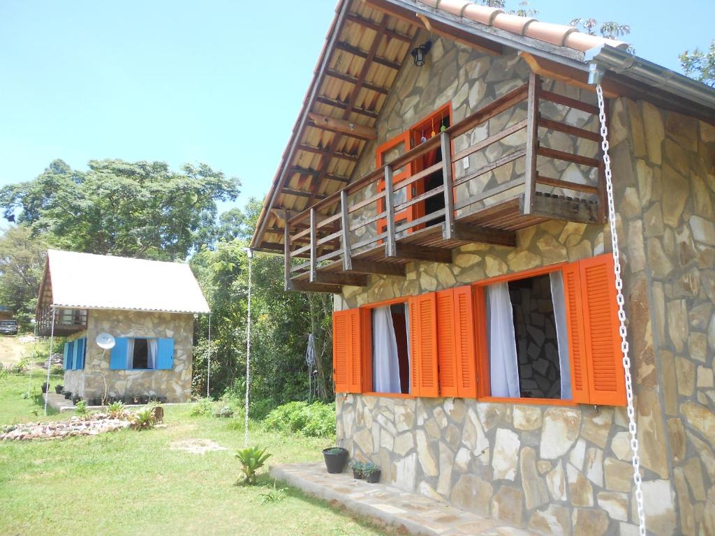 een stenen huis met oranje deuren en een balkon bij Repouso Sol in São Thomé das Letras