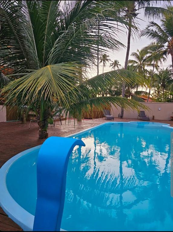 a blue swimming pool with palm trees in the background at Suíte Sol do Gostoso in São Miguel do Gostoso