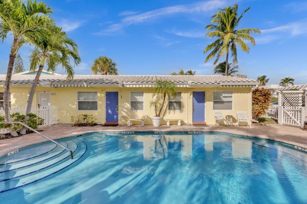 a swimming pool in front of a house with palm trees at Bahama Beach Club Pompano - Fort Lauderdale - Charming and Cozy Studios & Apartments close to Beach with heated Pool in Pompano Beach