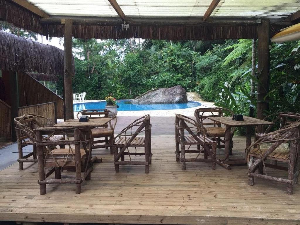 a wooden deck with tables and chairs and a pool at Pousada Toka do Lula - Oficial in Peruíbe
