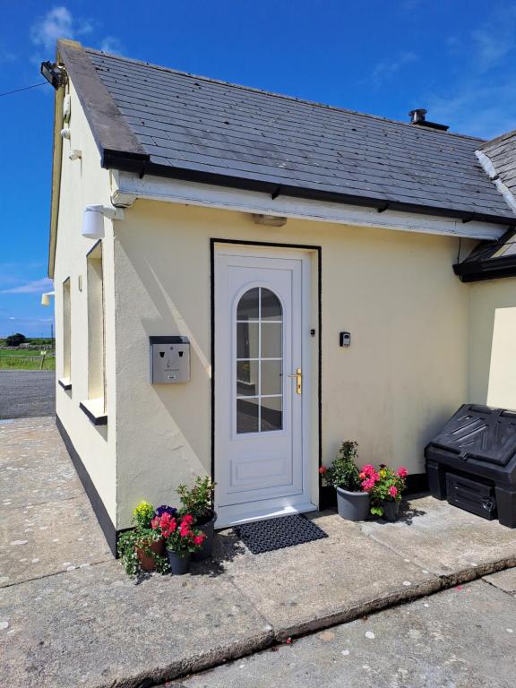 un pequeño edificio blanco con una puerta y flores en Doolin Farm Apartment, en Doolin