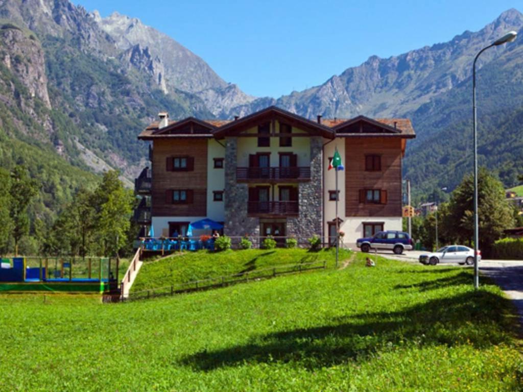 a large building on a hill with a green field at Casa Corti Ostello Ristorante in Valbondione