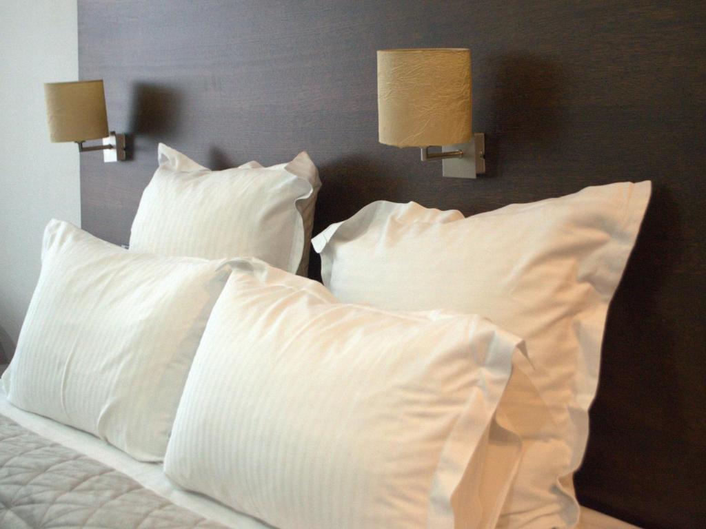 a bed with white pillows and two lights on it at Hotel EMD in Bacău