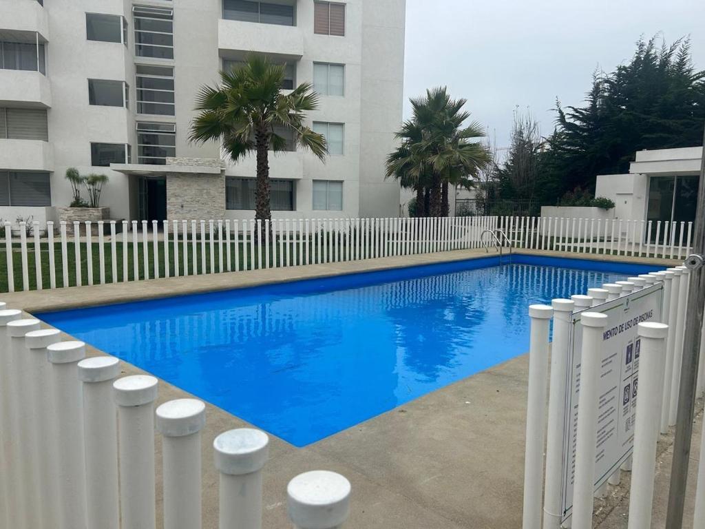a blue swimming pool next to a white fence at Acogedor departamento cerca de avenida del Mar in La Serena