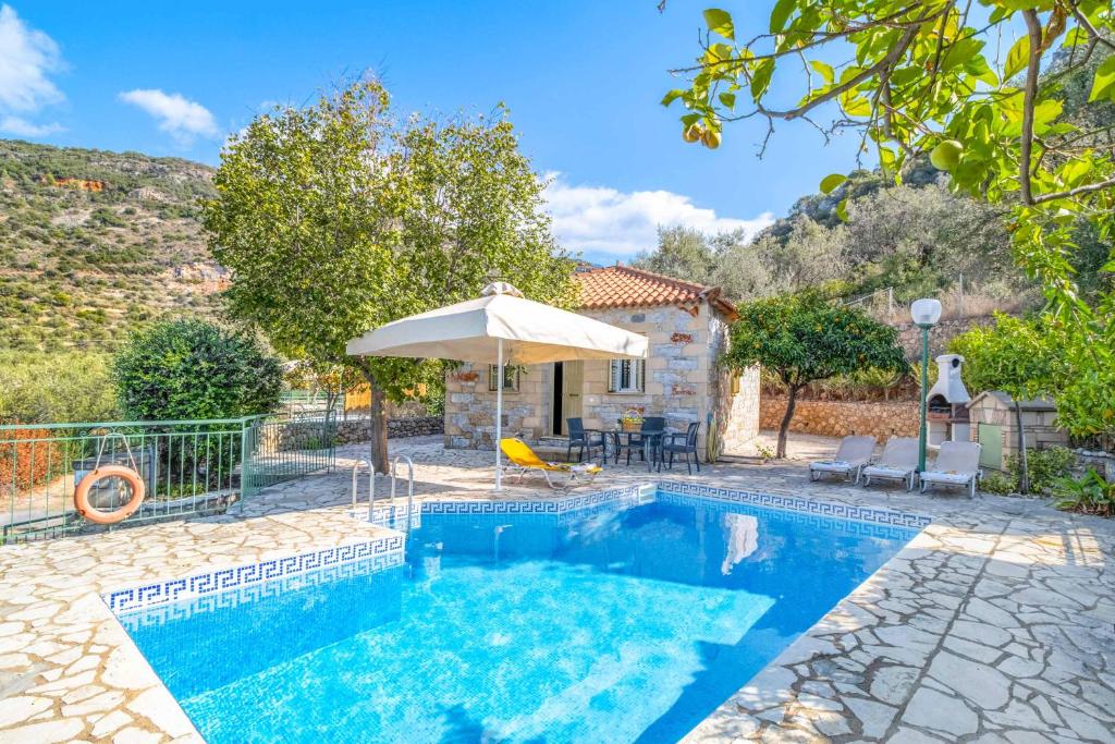 a swimming pool with an umbrella and a house at Villa Palataki II in Kardamyli