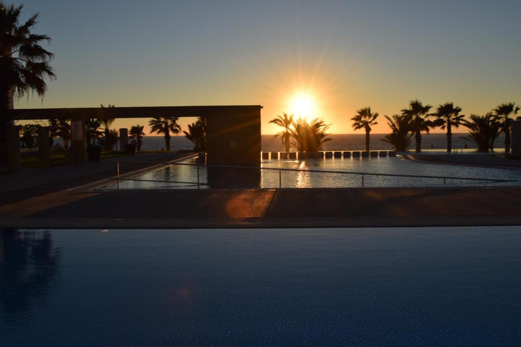 a sunset over a swimming pool with palm trees at Capital Coast Resort And Spa in Paphos City