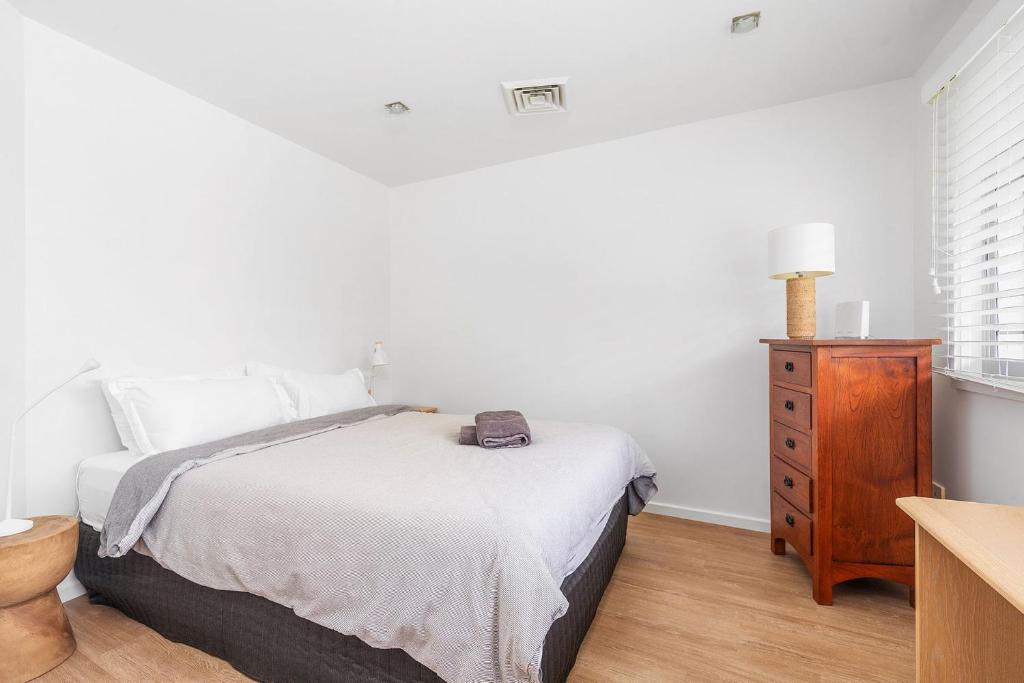 a white bedroom with a bed and a wooden dresser at Riverleigh, Gerroa in Gerroa