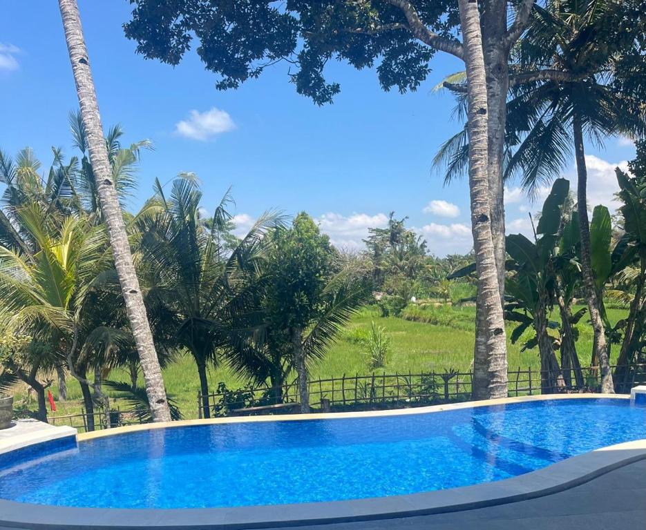 a swimming pool with palm trees in the background at Pondok Deamore Villa in Gianyar