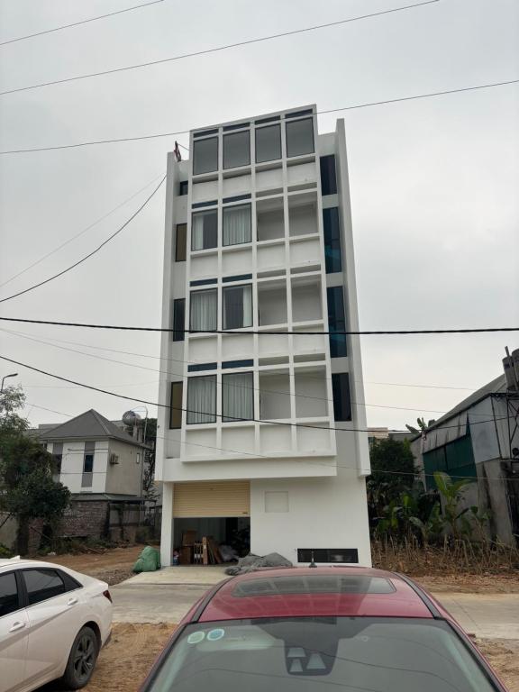 Un edificio alto y blanco con coches aparcados delante. en Bình Yên Hotel, en Thanh Ba