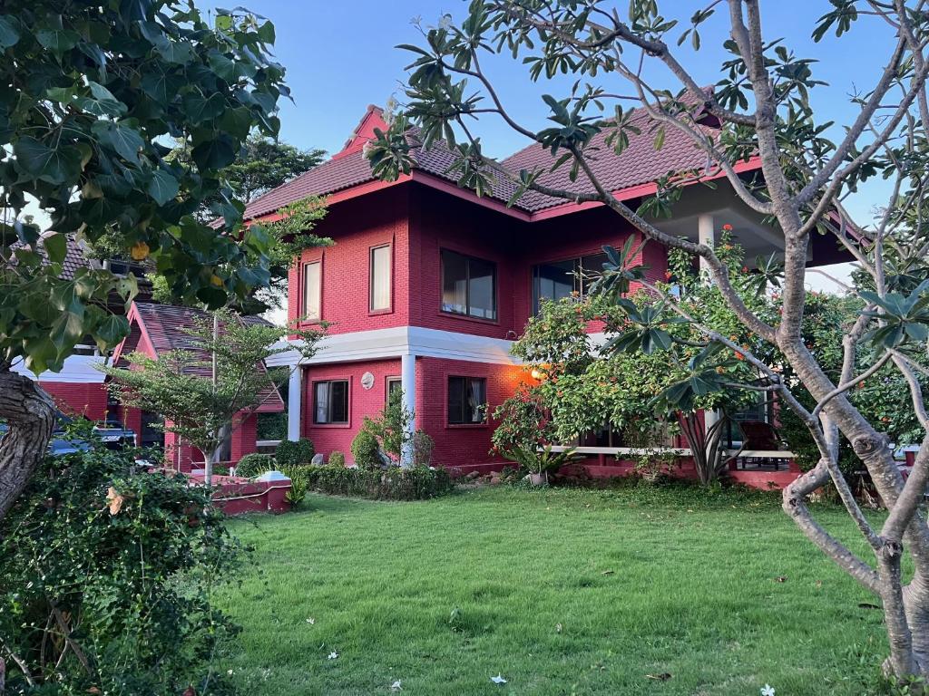 a red house with a lawn in front of it at Baan Plumeria บ้านภูมิเรีย in Phetchaburi