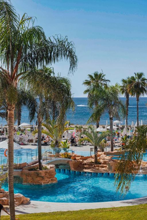 a view of a resort pool with palm trees and the ocean at Leonardo Cypria Bay in Paphos