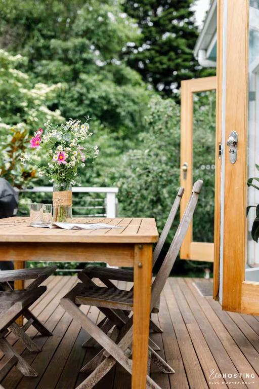 a wooden table with a vase of flowers on a deck at Tranquil Blue Cottage Close to Eco Point in Katoomba