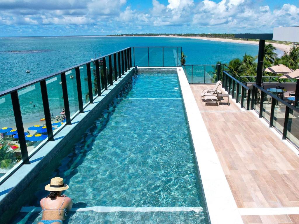 a woman in a hat sitting in a swimming pool overlooking the ocean at Beira-mar c/ Vista Mar | TKTU | Apt. 103 in Porto De Galinhas
