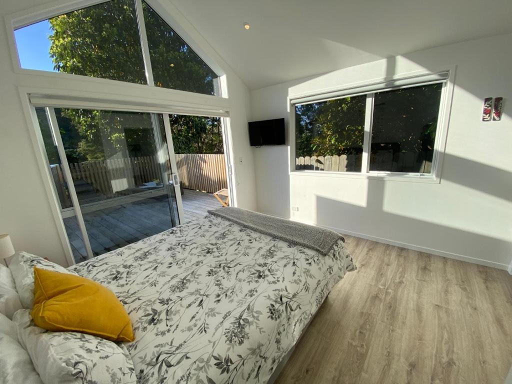 a bedroom with a bed and two large windows at Maraetai -Kererū Cottage - Whole House in Maraetai
