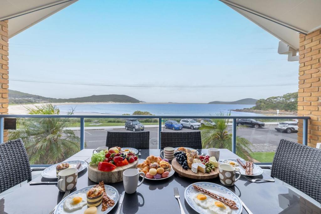 a table with breakfast food on a balcony with a view at Tah Villa 1, 68 Marine Dr - stunning views, linen and air con in Fingal Bay