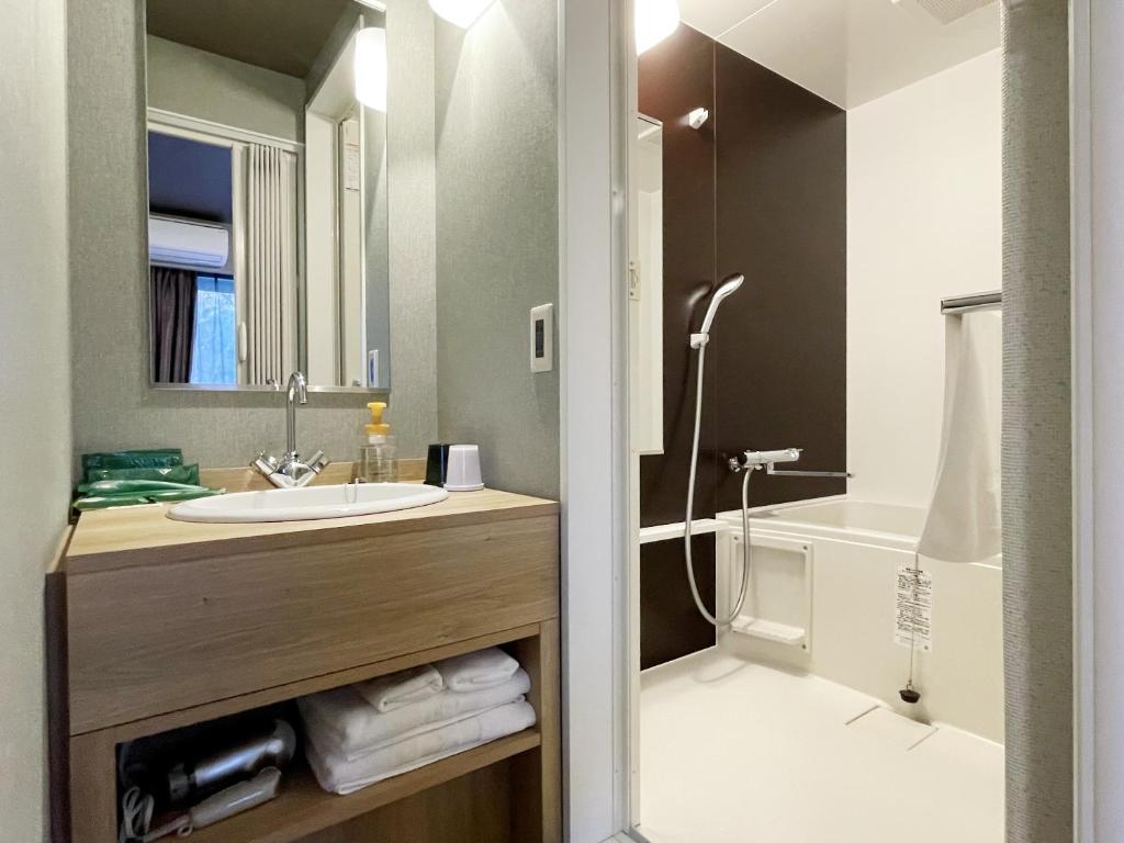 a bathroom with a sink and a mirror and a tub at Hotel Route-Inn Miyako in Miyako