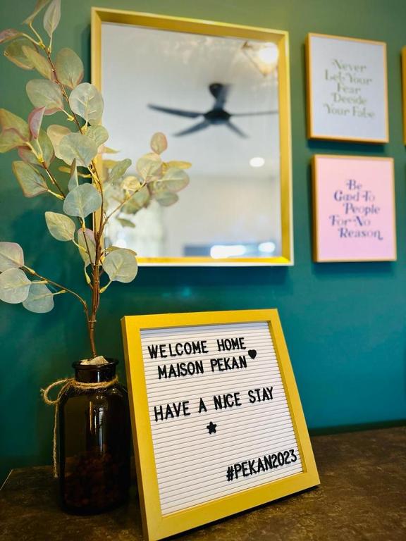 a sign on a table next to a vase with a plant at Maison Pekan in Pekan