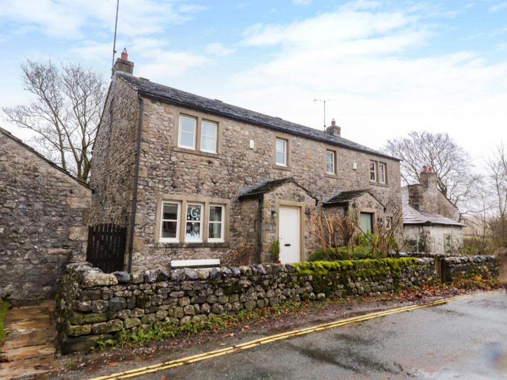 una antigua casa de piedra con un muro de piedra en Woodside Cottage, en Skipton