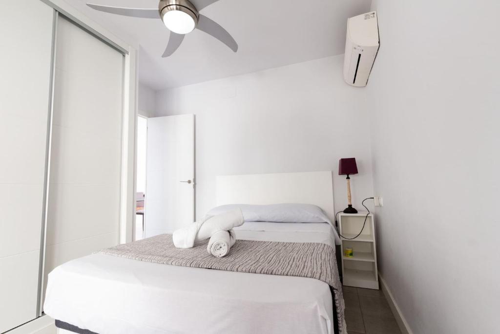 a white bedroom with a bed and a ceiling fan at Ático a pie de playa para relax y teletrabajo in Santa Pola