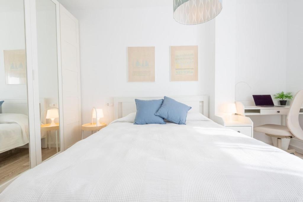 a white bedroom with a large white bed with blue pillows at Balcón Mediterráneo - Desconexión a pie de playa in Santa Pola