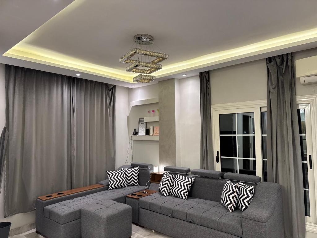 una sala de estar con sofá gris y una habitación con ventanas en New Cairo Hotel Apartment, en Madīnat ash Shurūq