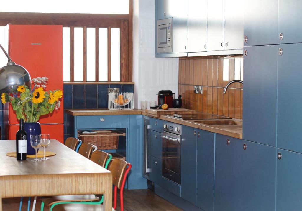 a kitchen with blue cabinets and a table with a vase of flowers at Eco Friendly beach house in Camber