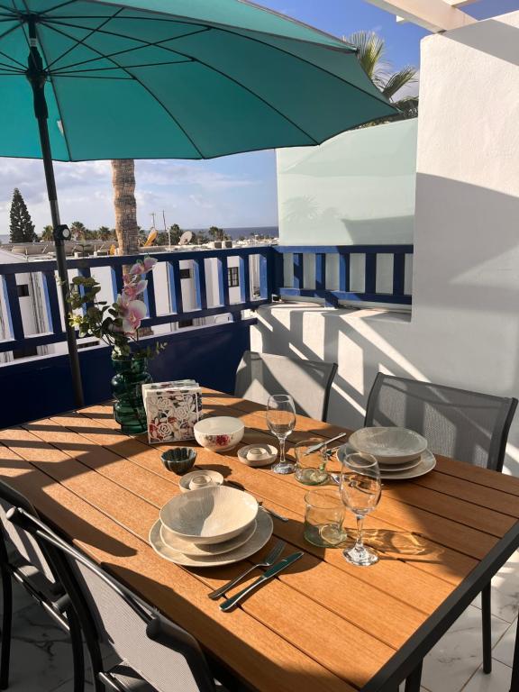 a wooden table with plates and glasses and an umbrella at TK OCEANVIEW Apartment in Puerto del Carmen